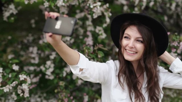 Happy woman taking selfie on tablet in the blooming garden.