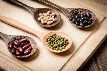 four colored beans  in wooden spoon on wood block