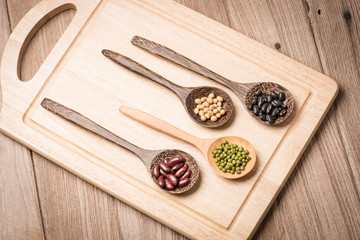 four colored beans  in wooden spoon on wood block