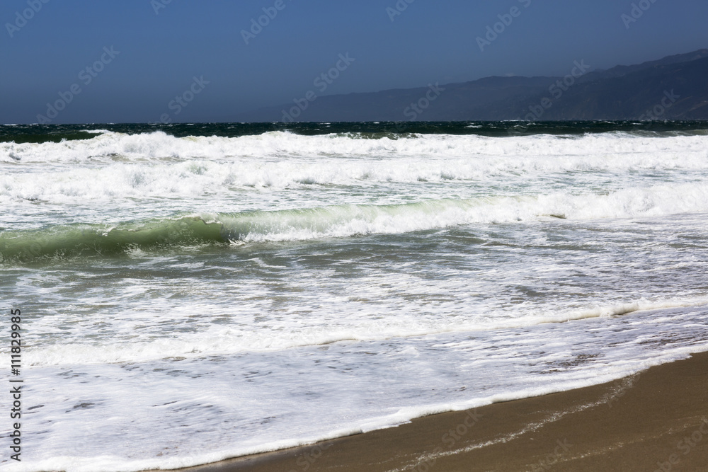 Wall mural The waves of the Pacific ocean, the beach landscape. The ocean, mountains and blue sky in USA, Santa Monica. The ocean and waves during strong winds in United States, Santa Monica.