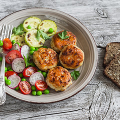 Chicken cutlets, grilled zucchini and fresh vegetable salad on rustic light wood background