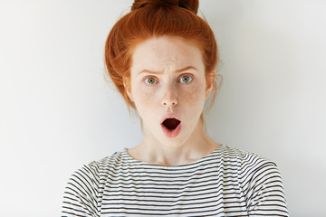 Portrait of stunned redhead freckled young female looking at the camera with shocked expression, mouth wide open, surprised with unexpected news. Human face expressions and emotions