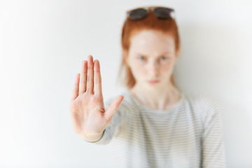 Isolated headshot of serious young redhead woman showing stop sign. Female wearing striped top looking at the camera with angry expression, gesturing with her palm. Selective focus. Film effect - obrazy, fototapety, plakaty