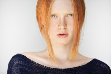 Headshot of teenage girl with red hair, blue eyes and smooth fresh clean skin, looking at the camera. Serious young female with ginger hair, wearing stylish black top. People and lifestyle concept.