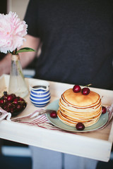 man holding a tray with breakfast of pancakes with cherry