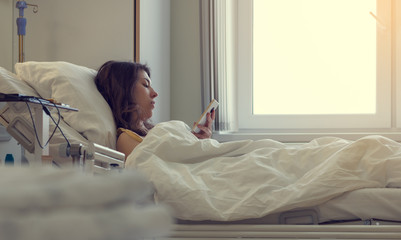 A sick patient lying in a hospital bed with a mobile phone.