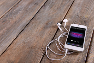 White smart phone with headphones on wooden background