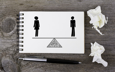 Equality of man and woman. On a wooden table notebook - obrazy, fototapety, plakaty