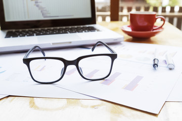 Office workplace with laptop and glasses on wood table.