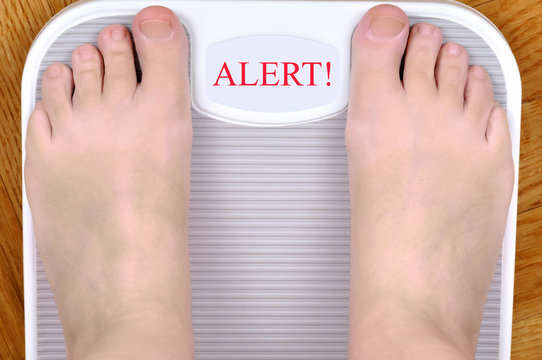 Barefoot Person Standing On The Weight Scale. The Scale Shows ALERT! 