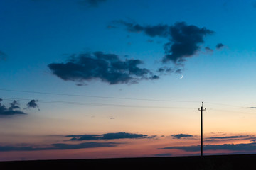 Fototapeta na wymiar electric pole on the background of sunset sky with clouds and moon