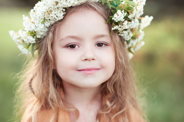 Cute kid girl 4-5 year old with flowers in hairstyle outdoors. Looking at camera. Childhood.