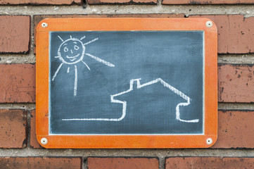Tafel an einer Ziegelwand mit einem Haus und Sonne / Tafel an einer Ziegelwand mit einer...