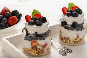 Healthy yogurt dessert with muesli, strawberries, blackberries and  blueberries on white wooden table.
