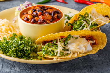 Tacos with chili con carne, salad, cheese and sour cream.