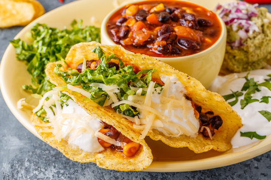Tacos with chili con carne, salad, cheese and sour cream.