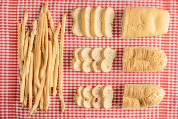 Composition of loaves and breatsticks over red and white checker table cloth with bread slices view from above