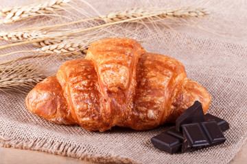 Tasty croissant with chocolate on rustic background with spikelets. Pastries and bread in a bakery