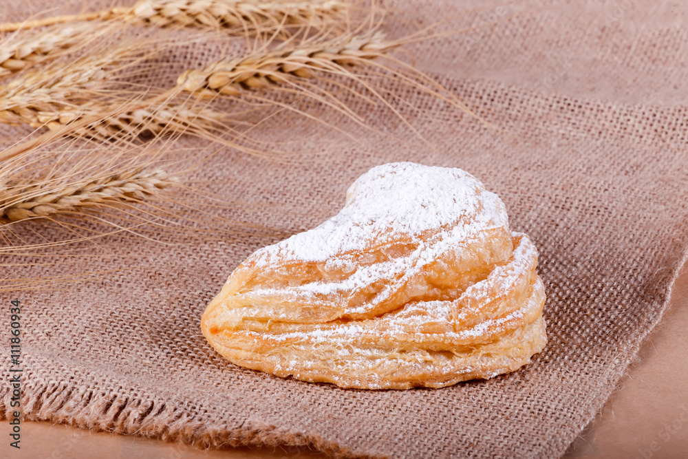 Wall mural Fresh puff pastry with powdered sugar on rustic background with spikelets. Pastries and bread in a bakery