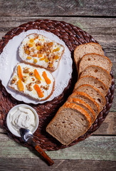 Sandwiches of rye bread with cream cheese, dried fruits, nuts, honey, cinnamon on the plate on rustic wooden background. Top view