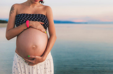 Young happy pregnant woman at the beach at sunset