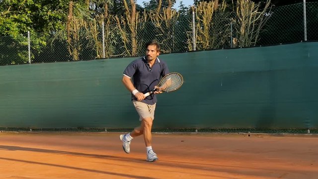 man tennis player hitting ball backhand  on a red clay court slow motion