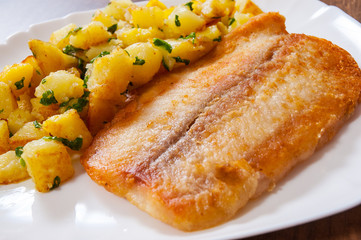 Fried fish fillet and potatoes in a plate on wooden table