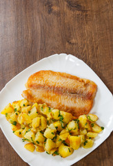 Fried fish fillet and potatoes in a plate on wooden table