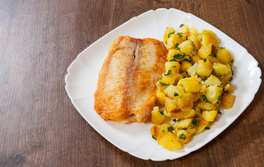 Fried fish fillet and potatoes in a plate on wooden table