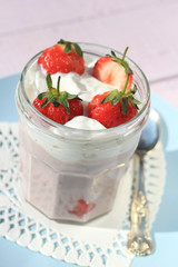 Fresh strawberries with fruit yoghurt and whipped cream on light pink wooden table