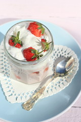 Fresh strawberries with fruit yoghurt and whipped cream on light pink wooden table
