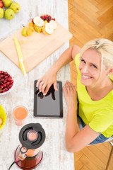 A beautiful mature woman with a smoothie in the kitchen using a tablet..