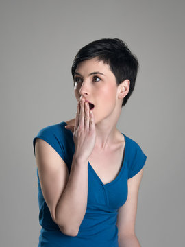 Portrait of shocked woman with hand over mouth looking away over gray studio background.