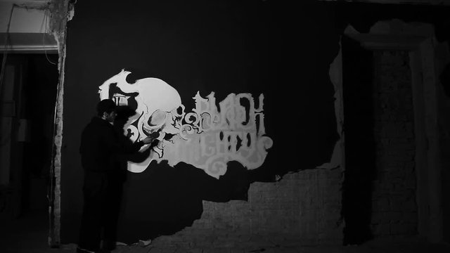 Artist painting white grafiti with skull on the black wall