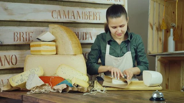 Young woman seller packs cheese, then smiling at the camera