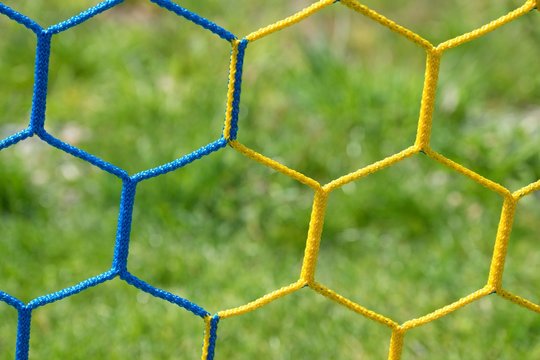 Detail of yellow blue crossed soccer football net with grass