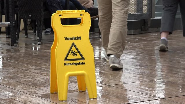 People walk past German caution sign in the rain
