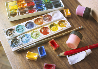 Boxes with watercolors on a wooden background, brushes, pencil