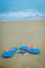 Fototapeta na wymiar Top view close up on mobile phone with slippers on summer beach background. Happy joyful vacation