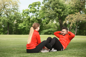 Fototapeta premium Sport man training in park doing abdominal crunches. Group of man and woman exercising on fresh air in green park or forest.