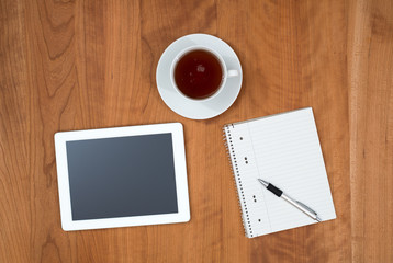 tablet PC and notepad and a cup of tea on wooden table from abov