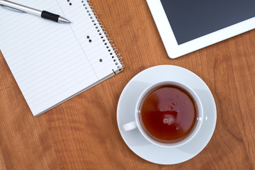tablet PC and notepad and a cup of tea on wooden table from abov