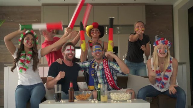 Enthusiastic Soccer Fans Watching Tv At Home Cheering For Different European Teams
