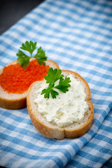 Bread with fresh cream cheese and red caviar on table.