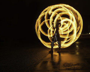 Fire stick artist performs on a wet pavement at night.