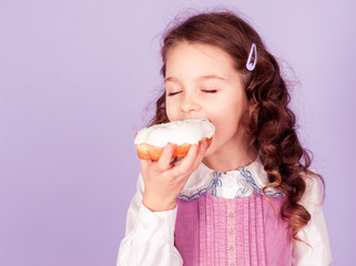 Smiling baby girl 4-5 year old eating donut in room. Childhood.