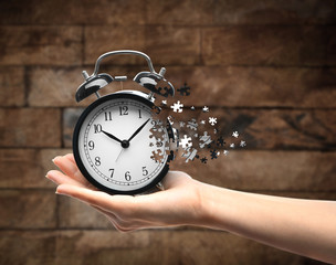 A retro alarm-clock on female hand on wooden background. Lost time concept