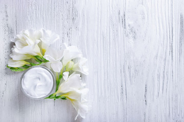 Moisturizing cream and flowers on white wooden background