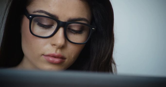 Beautiful brunette woman with brown hair and glasses using a laptop computer, close-up