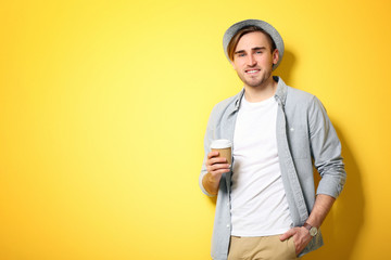 Young handsome man with a cup of coffee on bright yellow background